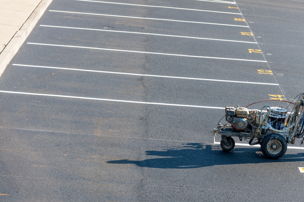 Worker painting fresh road striping lines at a new development site