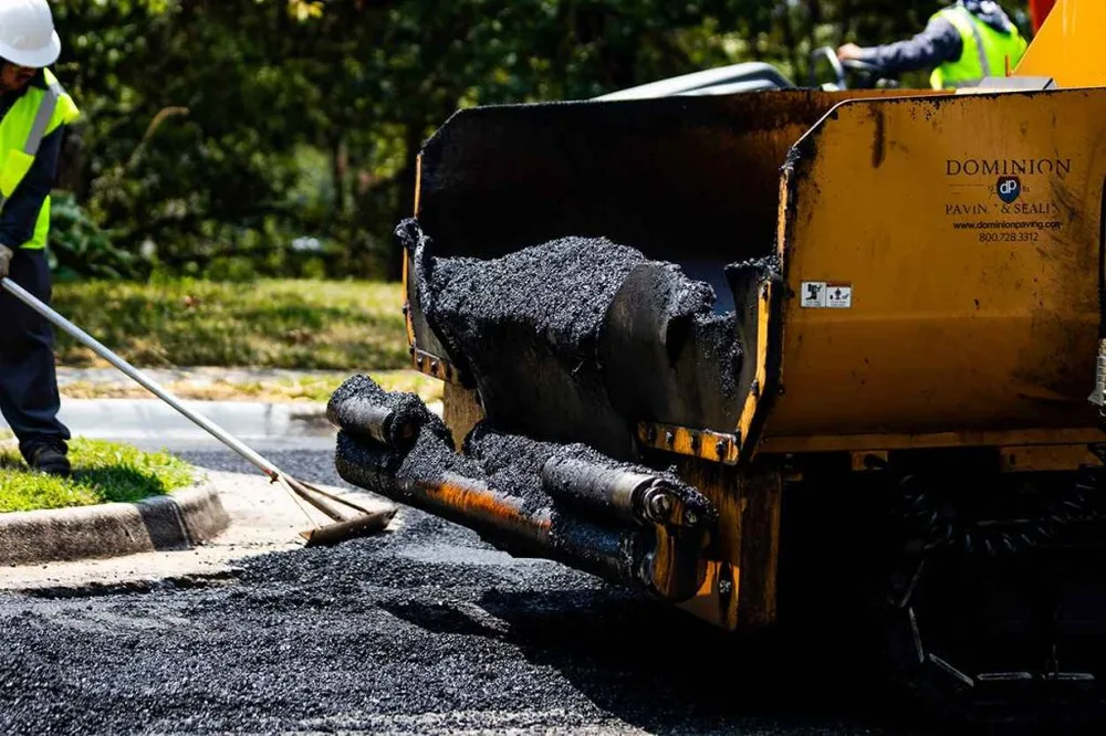 Dominion Paving Contractor Smoothing Surface While Asphalt is Being Poured Out From Truck